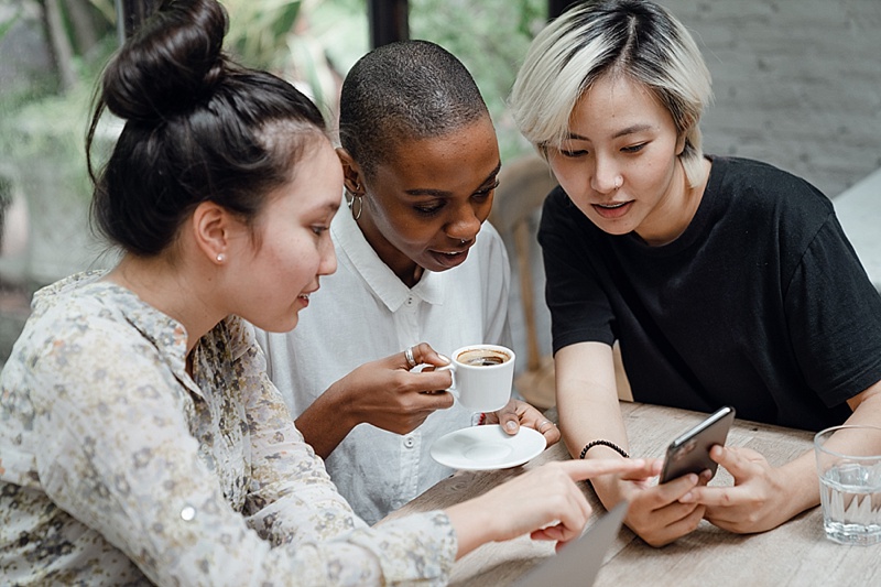 3 women looking at a phone over coffee